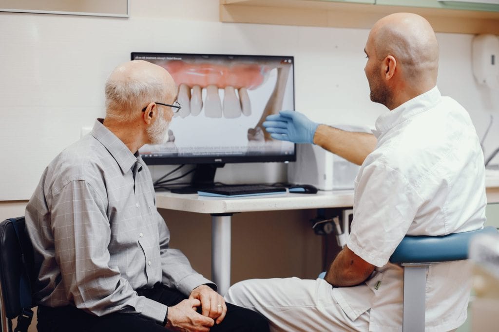 Sólo puedo describir esta imagen como un profesional de la odontología explicando una radiografía digital a un paciente mayor en consulta dental.